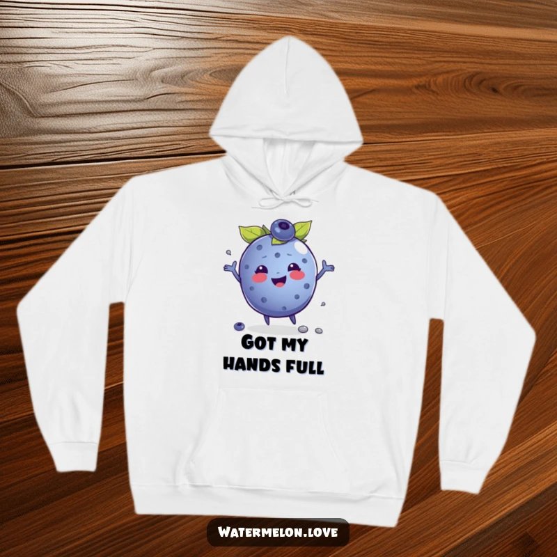 Funny hoodie featuring a gleeful anthropomorphic blueberry in the act of juggling seeds, offering cozy and cheerful vibes.